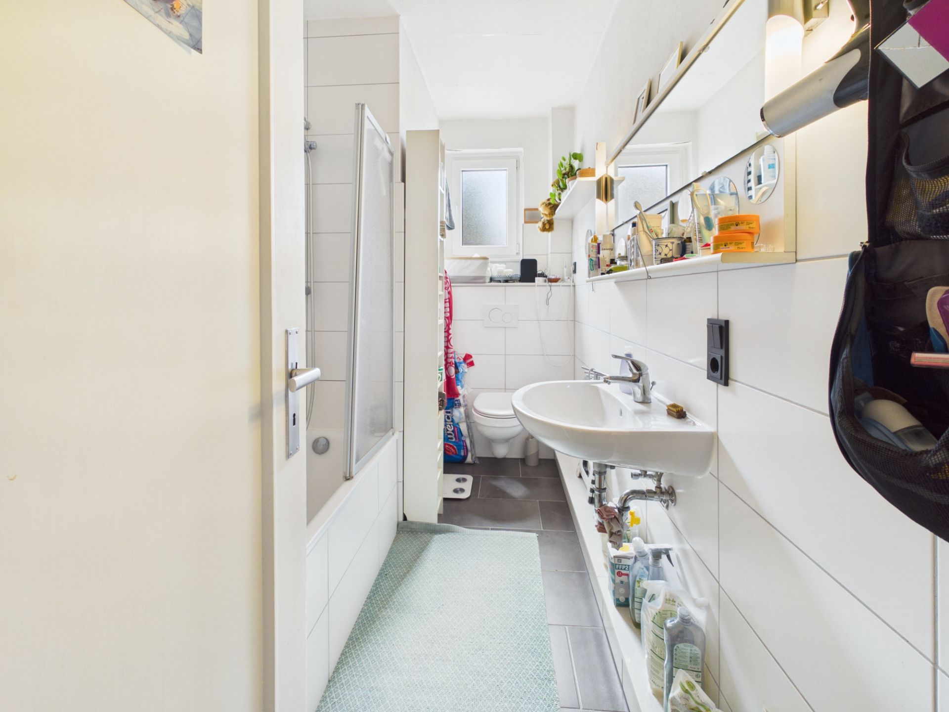 Helles Badezimmer mit Badewanne, Waschbecken, Spiegel und Fenster.