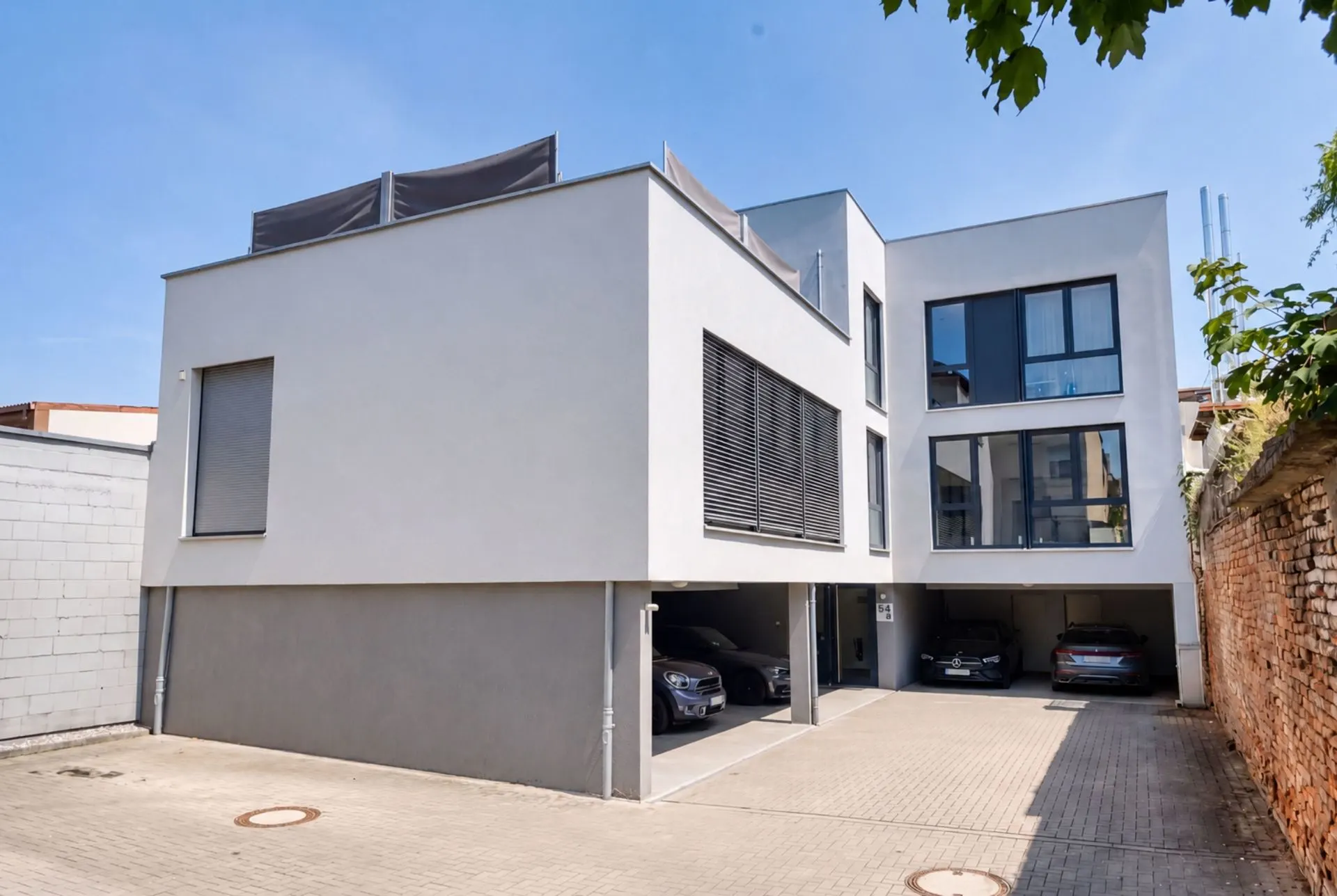 Modernes Wohngebäude mit großen Fenstern und Parkplätzen im Erdgeschoss.
