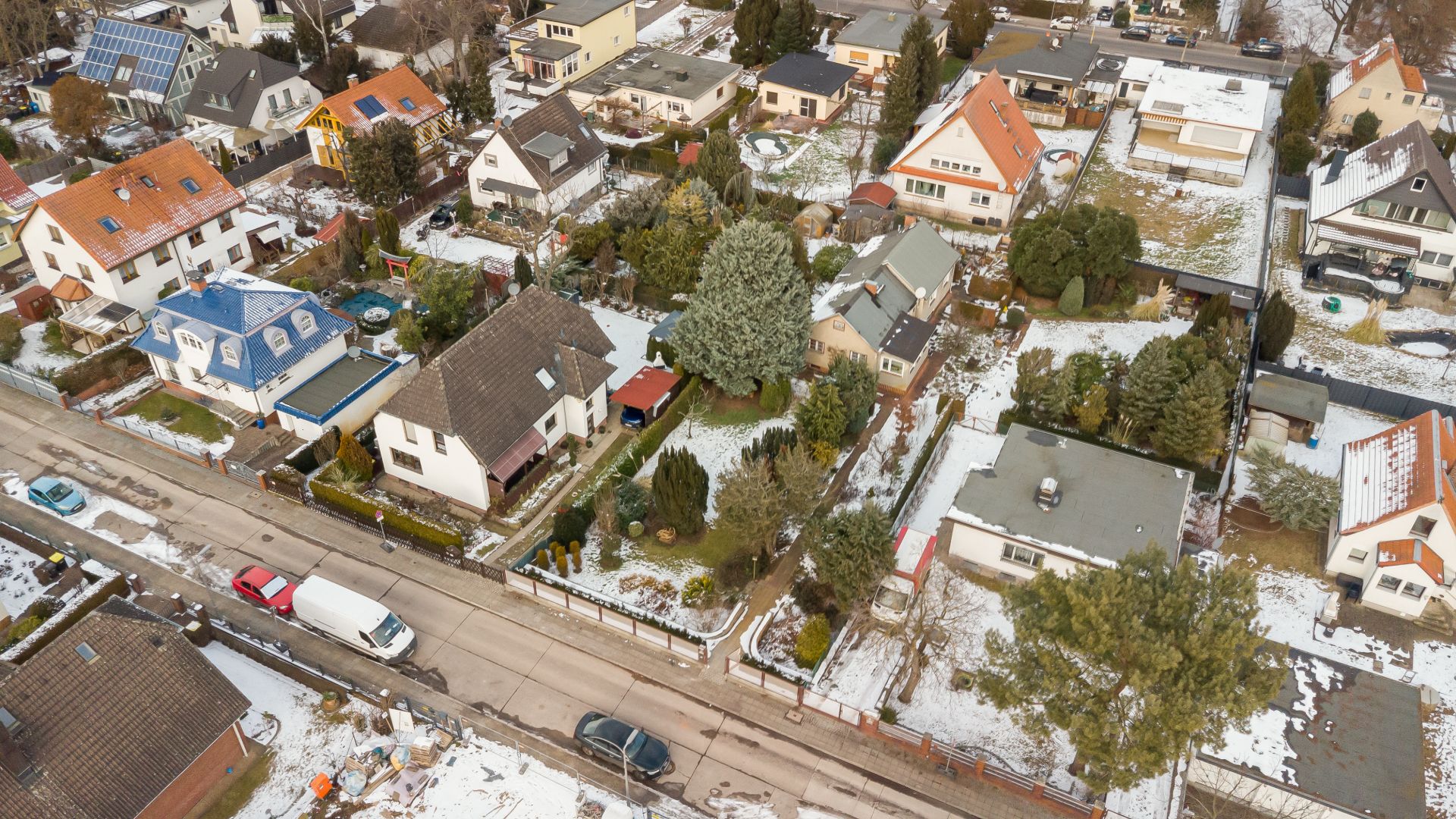 Luftaufnahme von Einfamilienhäusern mit Gärten und etwas Schnee auf den Dächern und Straßen.