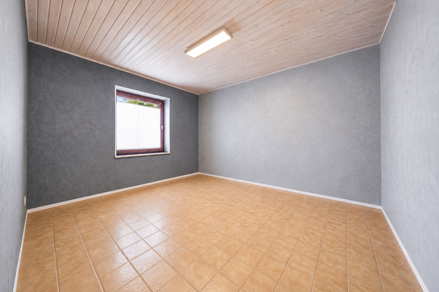 Leerer Raum mit Fliesenboden, grauen Wänden, Holzdecke und Fenster mit Jalousie.