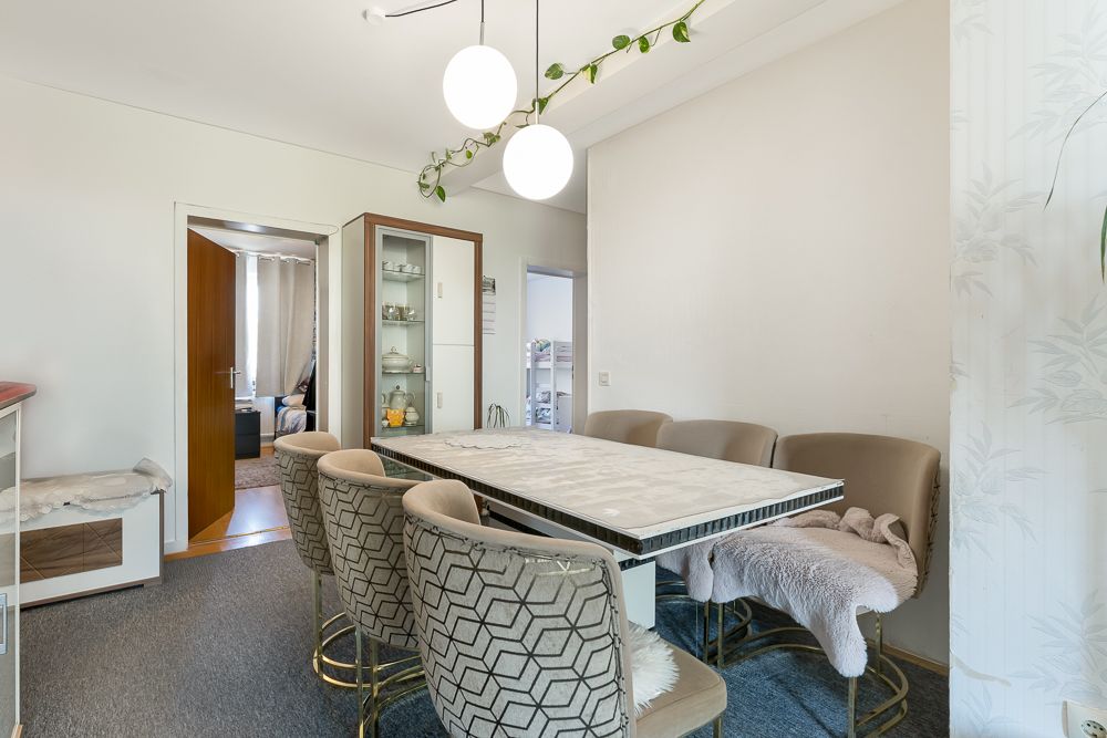 Esszimmer mit großem Tisch und sechs Polsterstühlen, modernes Licht mit Rundlampen an der Decke.