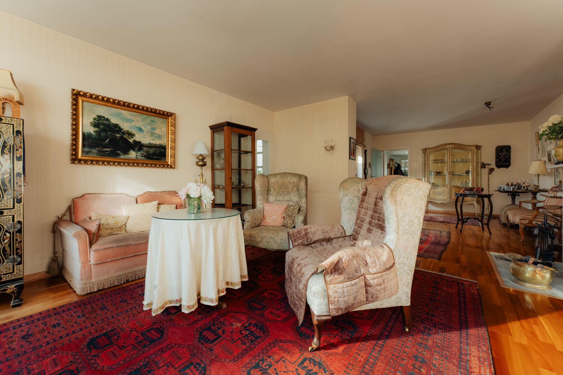 Wohnzimmer mit zwei Sesseln, einem Sofa, rundem Tisch, Teppich und Gemälde an der Wand.