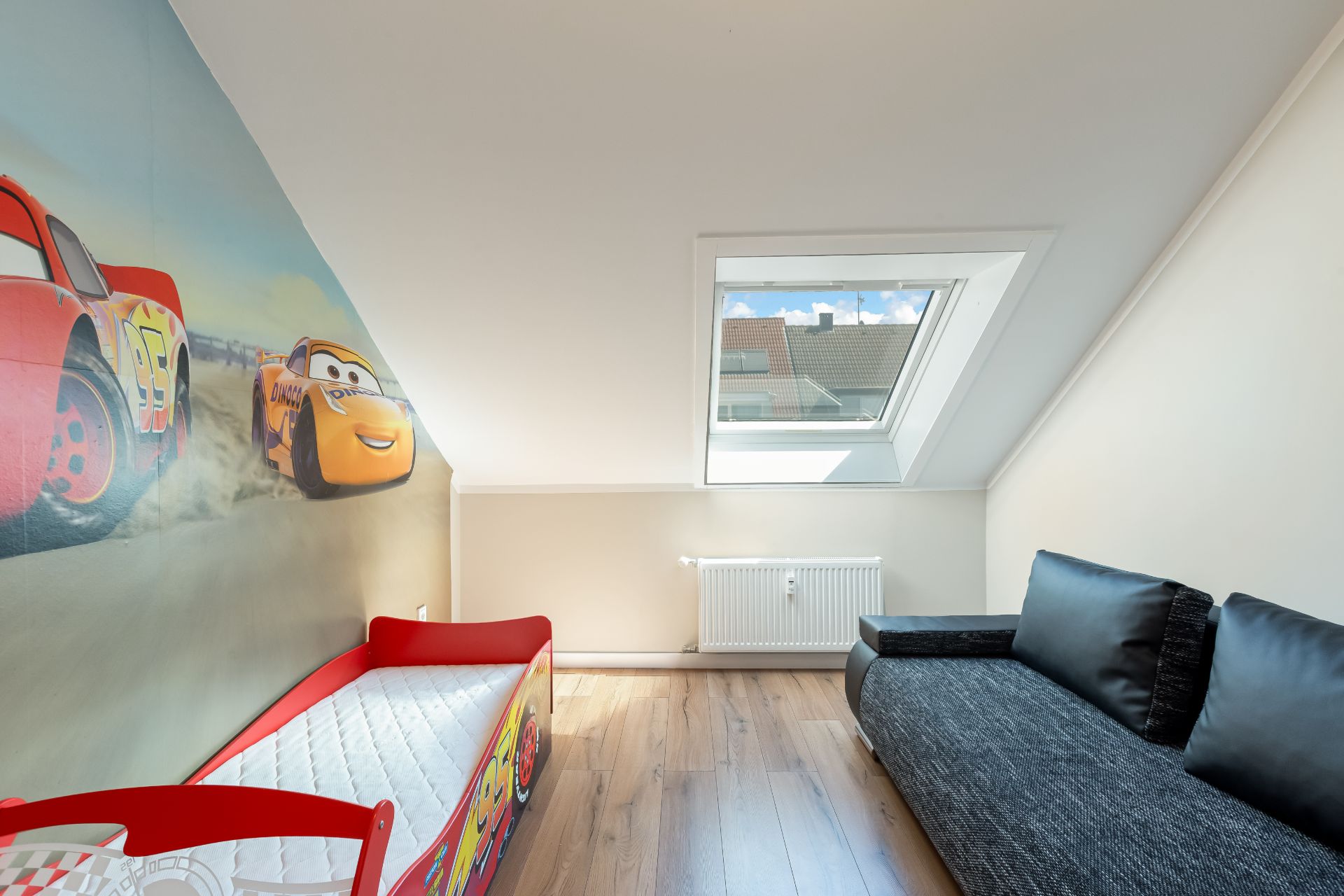 Kinderzimmer mit Dachfenster, Kinderbett mit Cars-Motiv und schwarzem Sofa.
