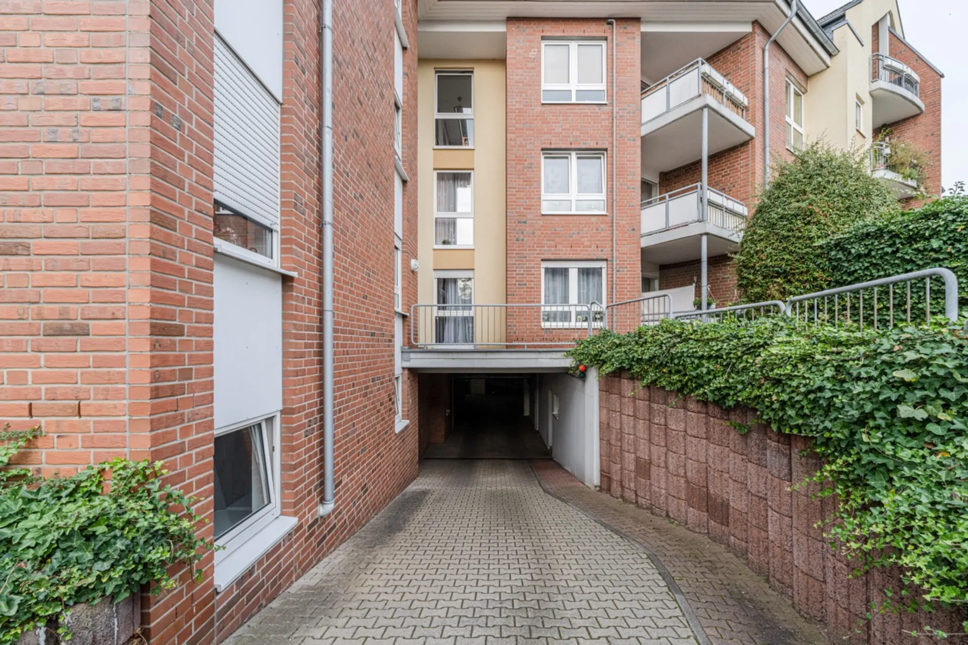 Einfahrt zur Tiefgarage eines Wohnhauses mit roten Ziegelwänden und begrünten Seiten.