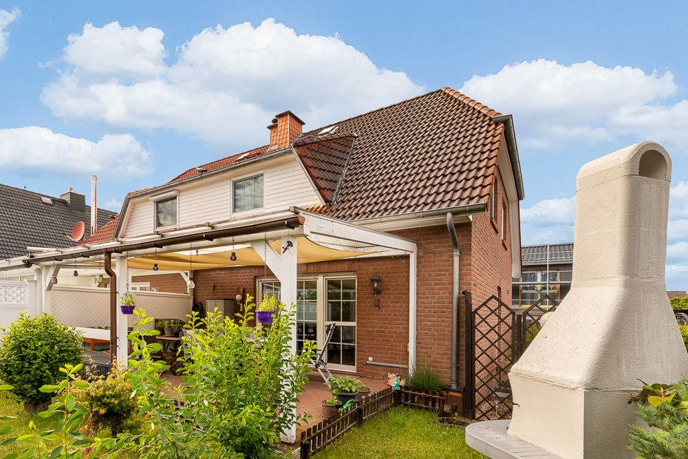 Backsteinwohnhaus mit überdachter Terrasse, Garten und gemauertem Grill im Vordergrund.