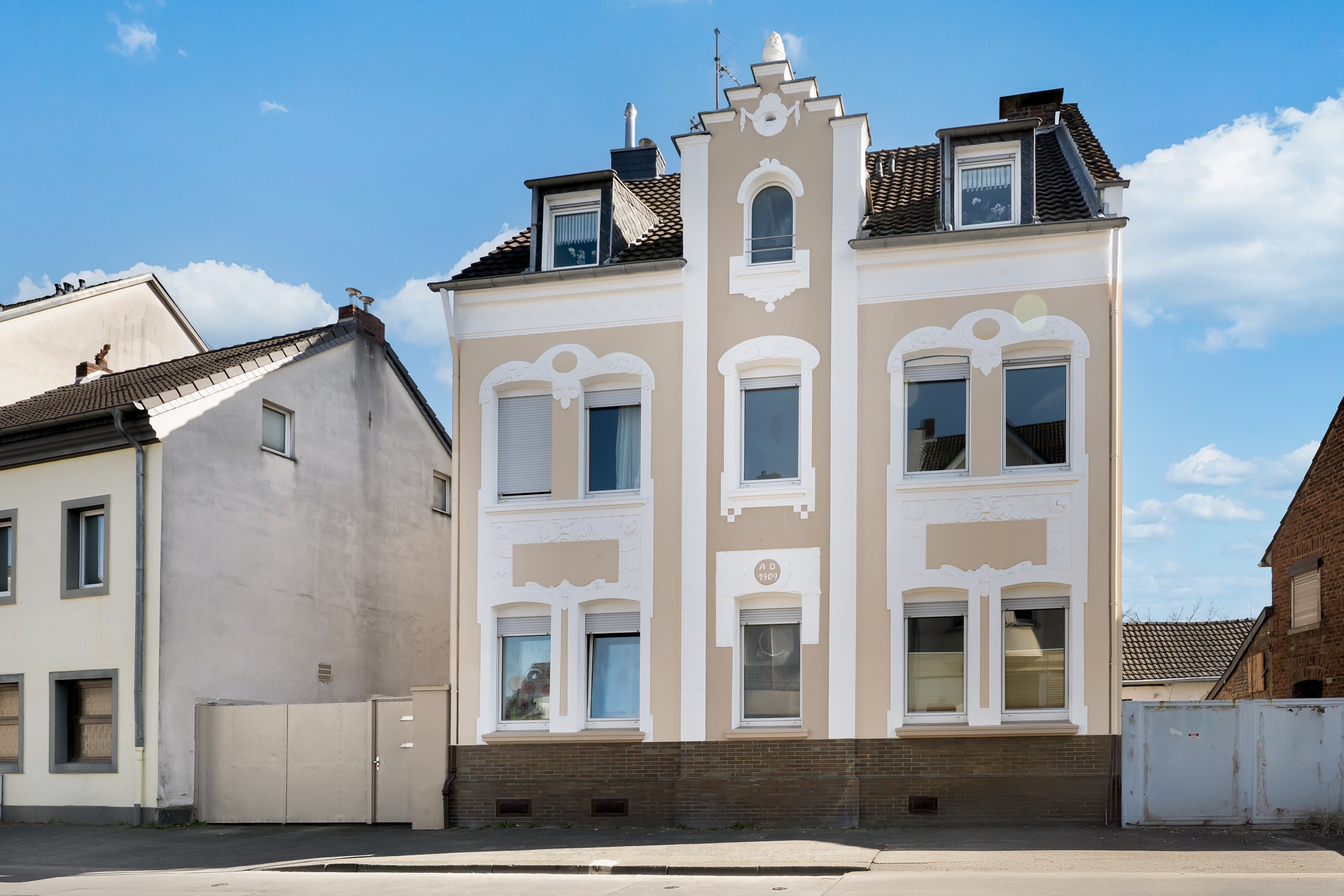 Zweistöckiges Wohnhaus mit Dachfenstern und dekorativen Fassadenelementen an einer Straße.