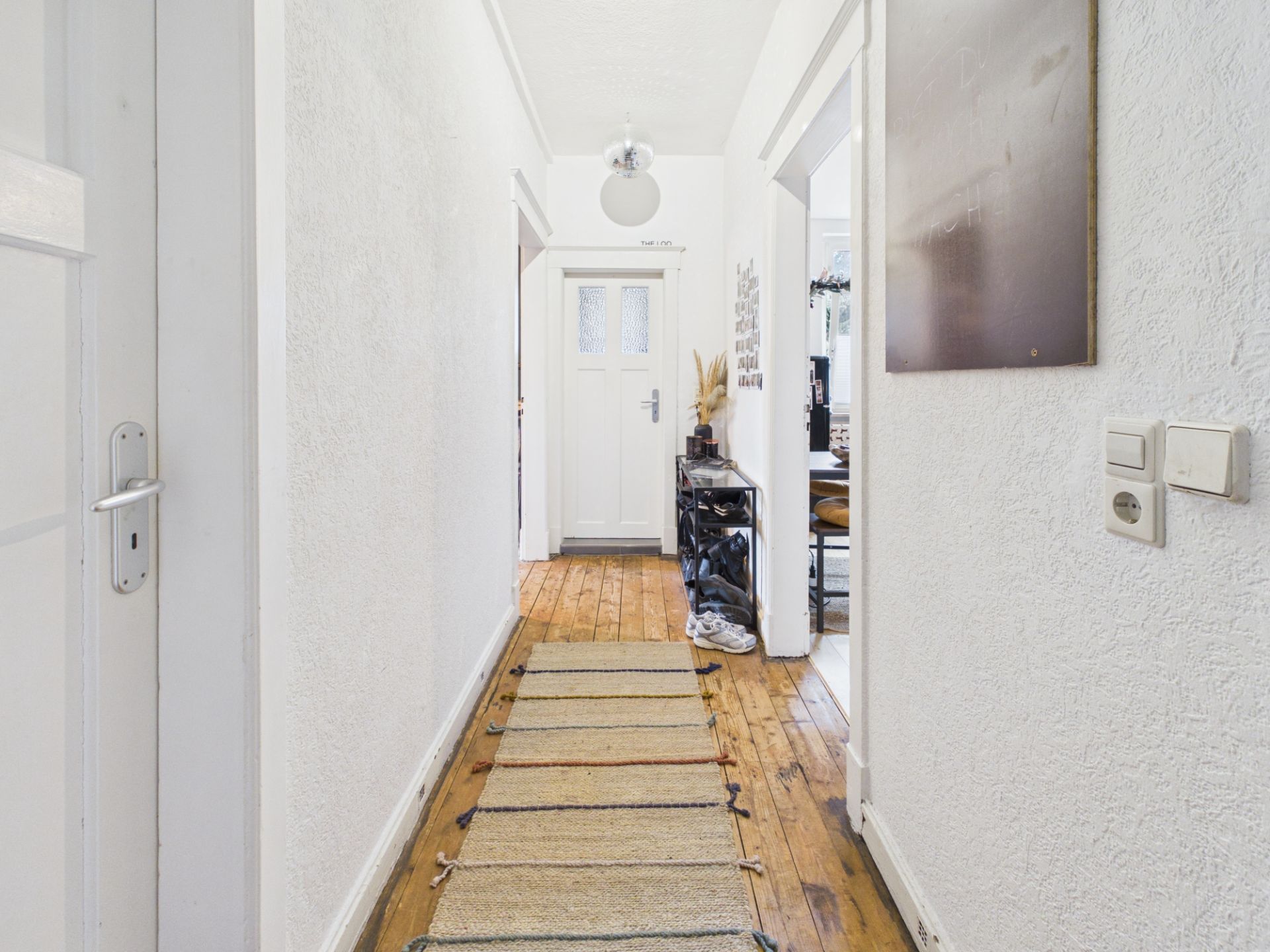 Heller Flur mit Holzboden, Teppichläufer und weißer Tür am Ende.