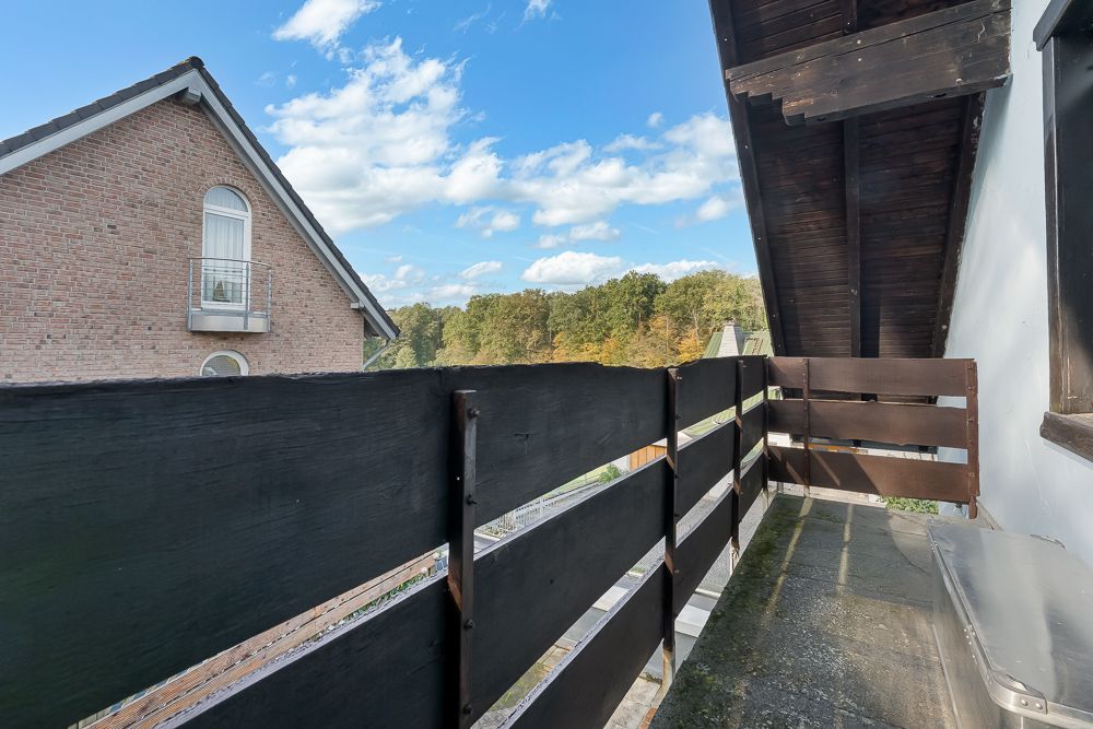 Kleiner Balkon mit dunklem Holzzaun, Blick auf Bäume und Nachbarhaus mit Backsteinfassade.