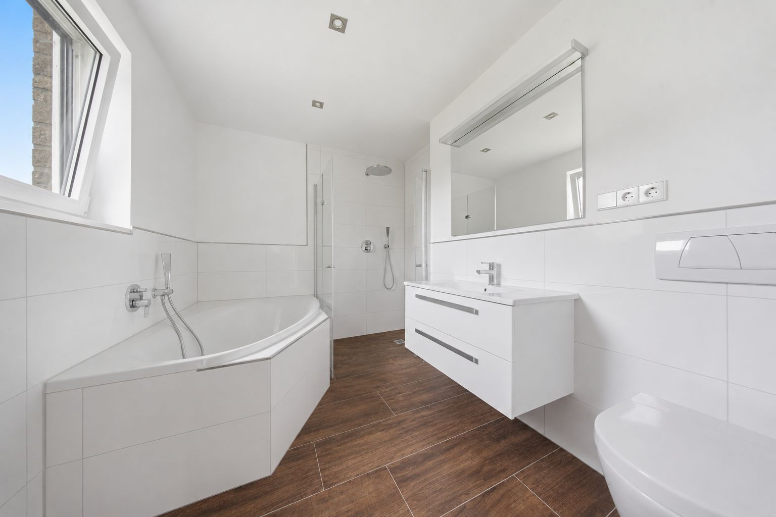 Modernes Badezimmer mit Badewanne, Dusche, Waschbecken und WC, brauner Boden, weiße Wände.