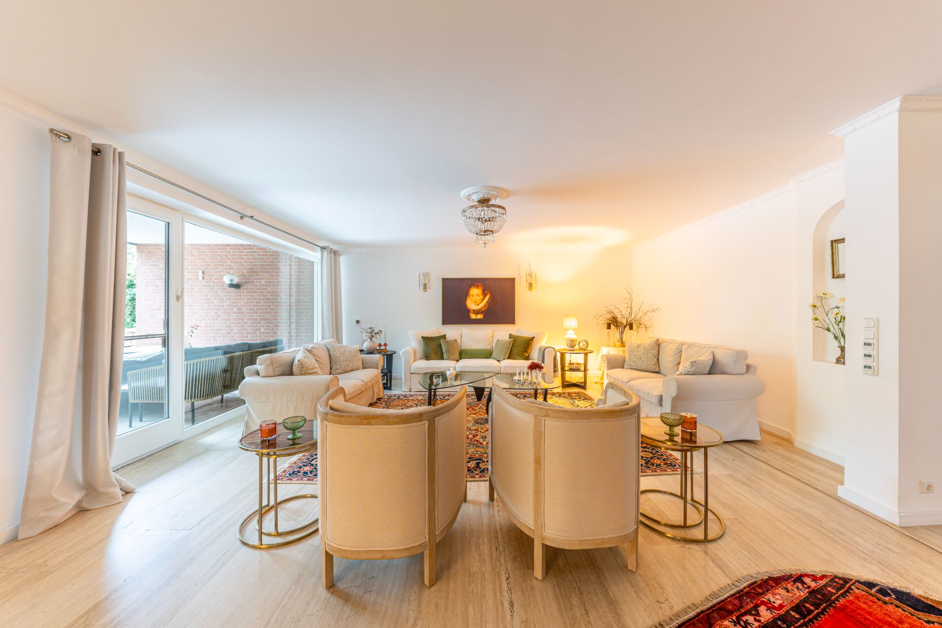 Helles Wohnzimmer mit mehreren Sofas, Sesseln, Teppichen und einem großen Fenster zur Terrasse.