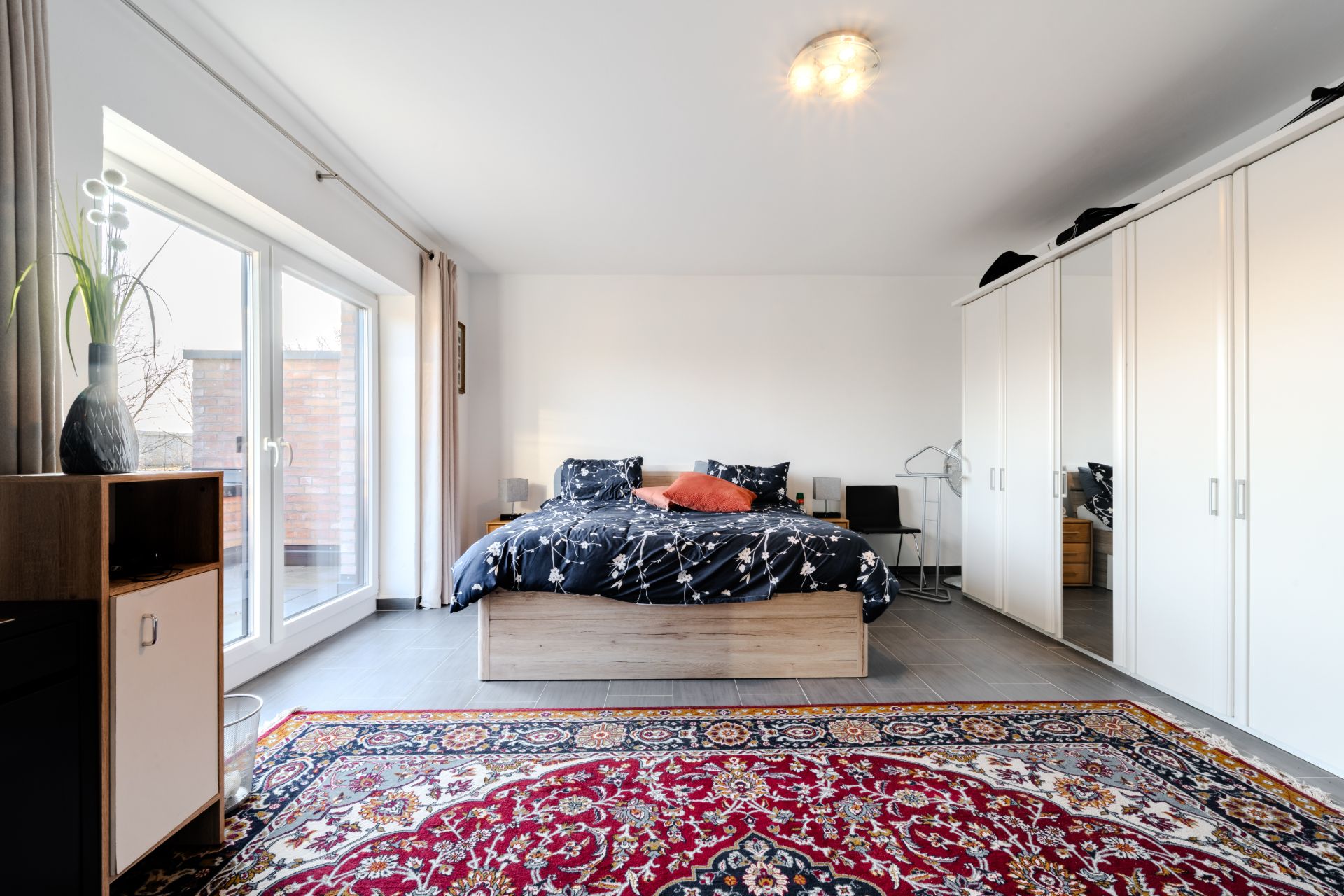 Helles Schlafzimmer mit Doppelbett, großem Teppich und weißen Einbauschränken.