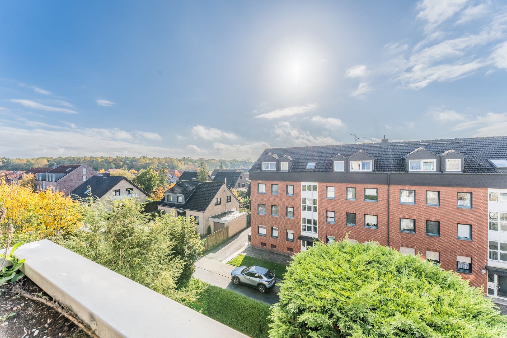 Blick auf Wohnhäuser, Bäume und ein geparktes Auto bei sonnigem Wetter.