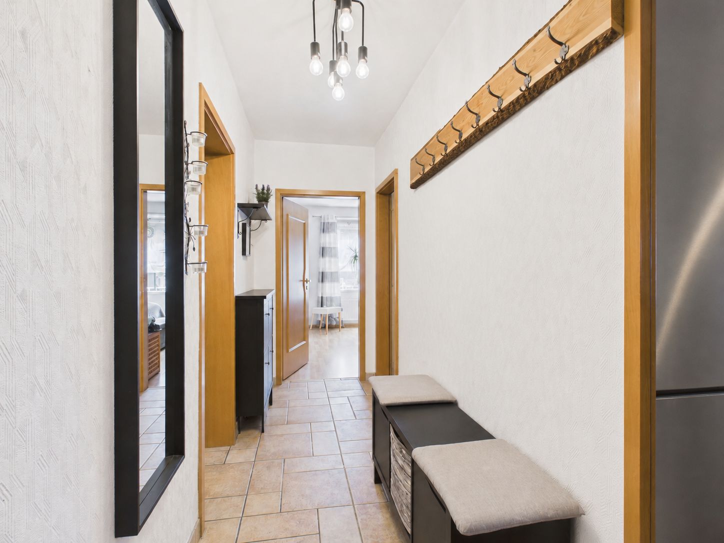 Heller Flur mit Spiegel, Sitzbank, Garderobe und Fliesenboden in einer Wohnung.