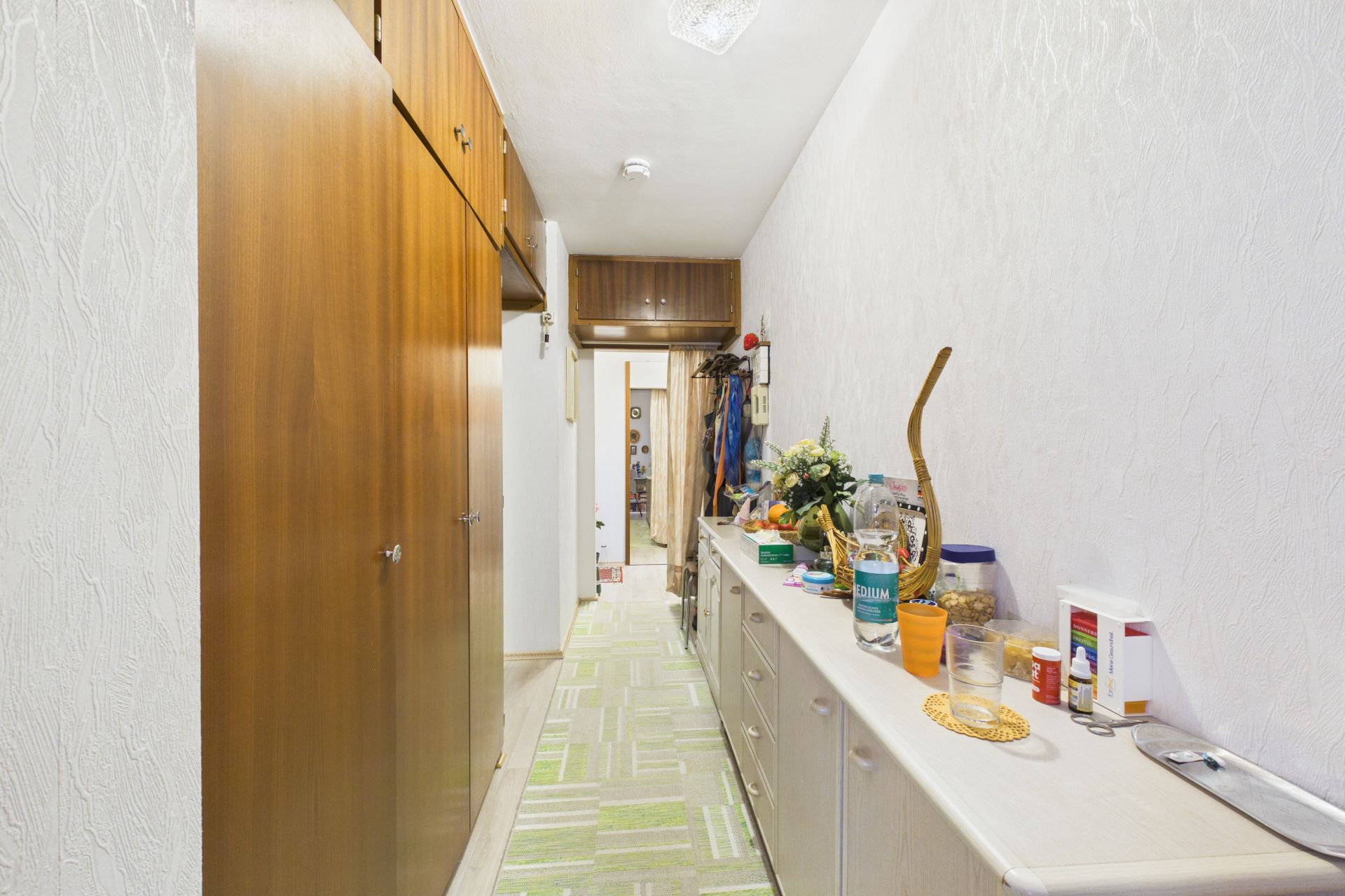 Langer Flur mit Einbauschränken aus Holz und Sideboard mit diversen Gegenständen.