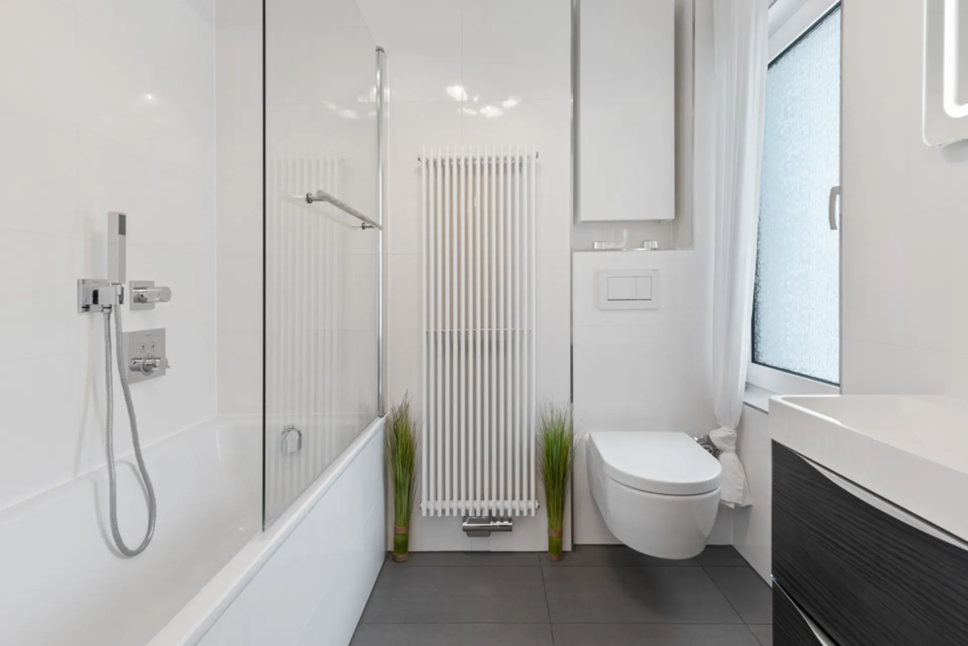 Modernes Badezimmer mit Badewanne, wandhängender Toilette, Waschbecken und großem Fenster.