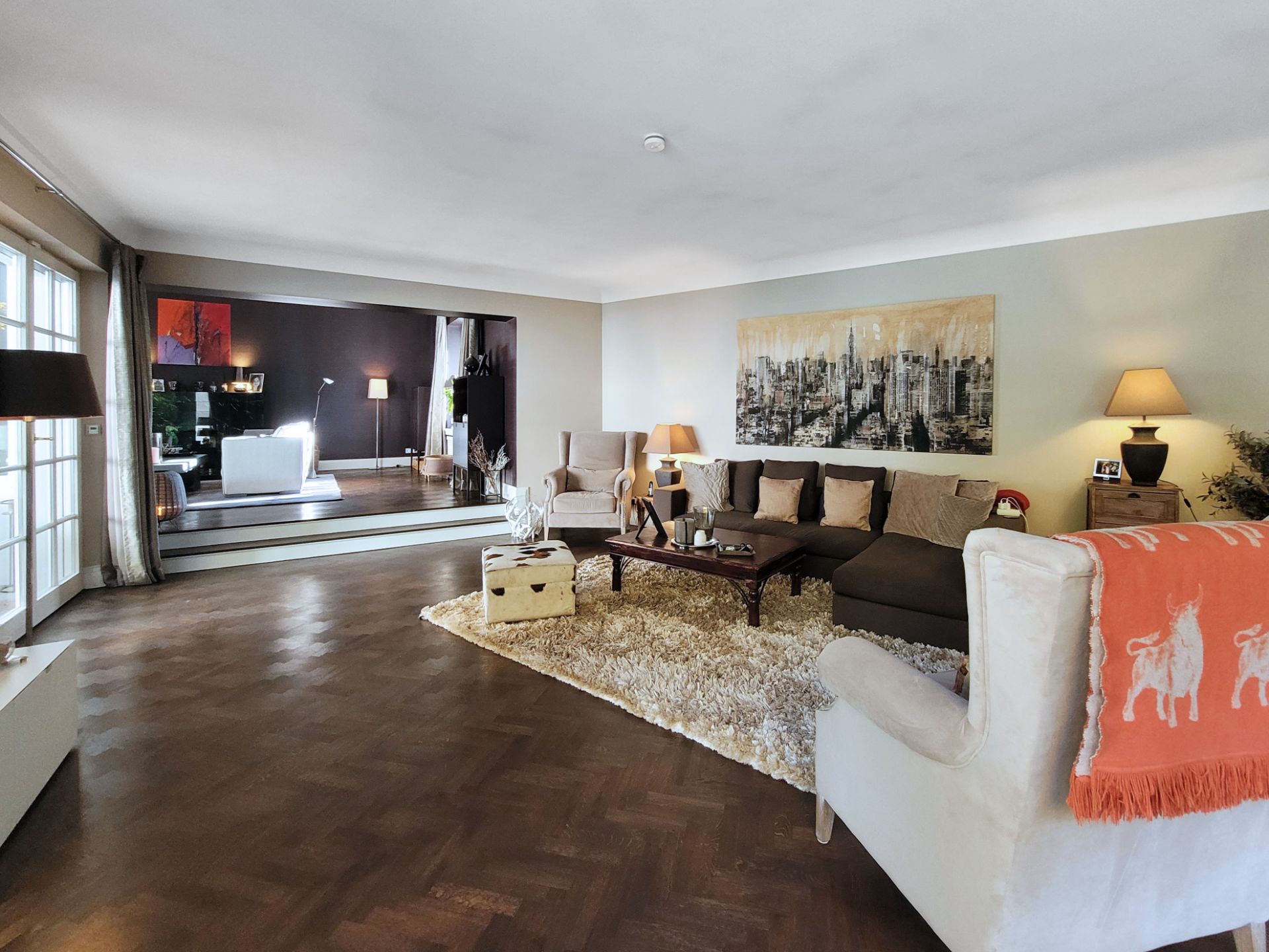 Großes Wohnzimmer mit Sofa, Sesseln, Teppich, Couchtisch und Wandbild.