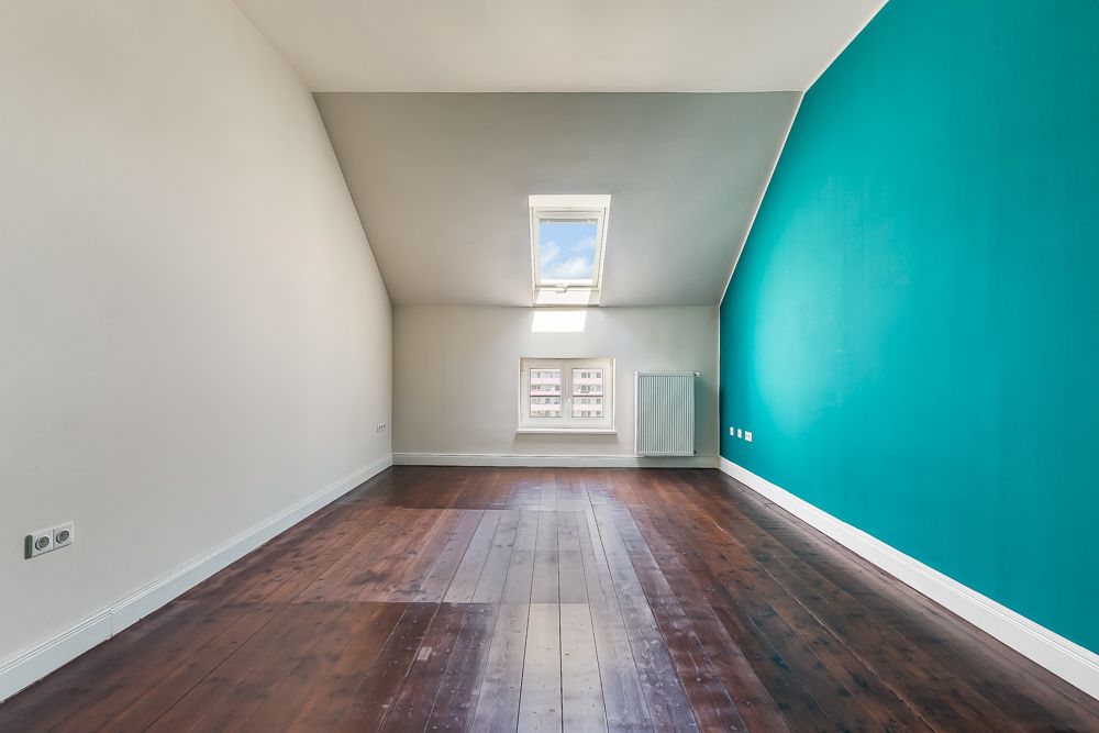 Leerer Raum mit Holzboden, weißer Schräge, türkisfarbener Wand und Dachfenster.