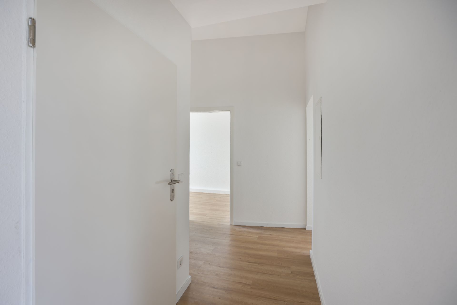 Heller Flur mit Holzboden und einer offenen Tür zu einem weiteren Raum.