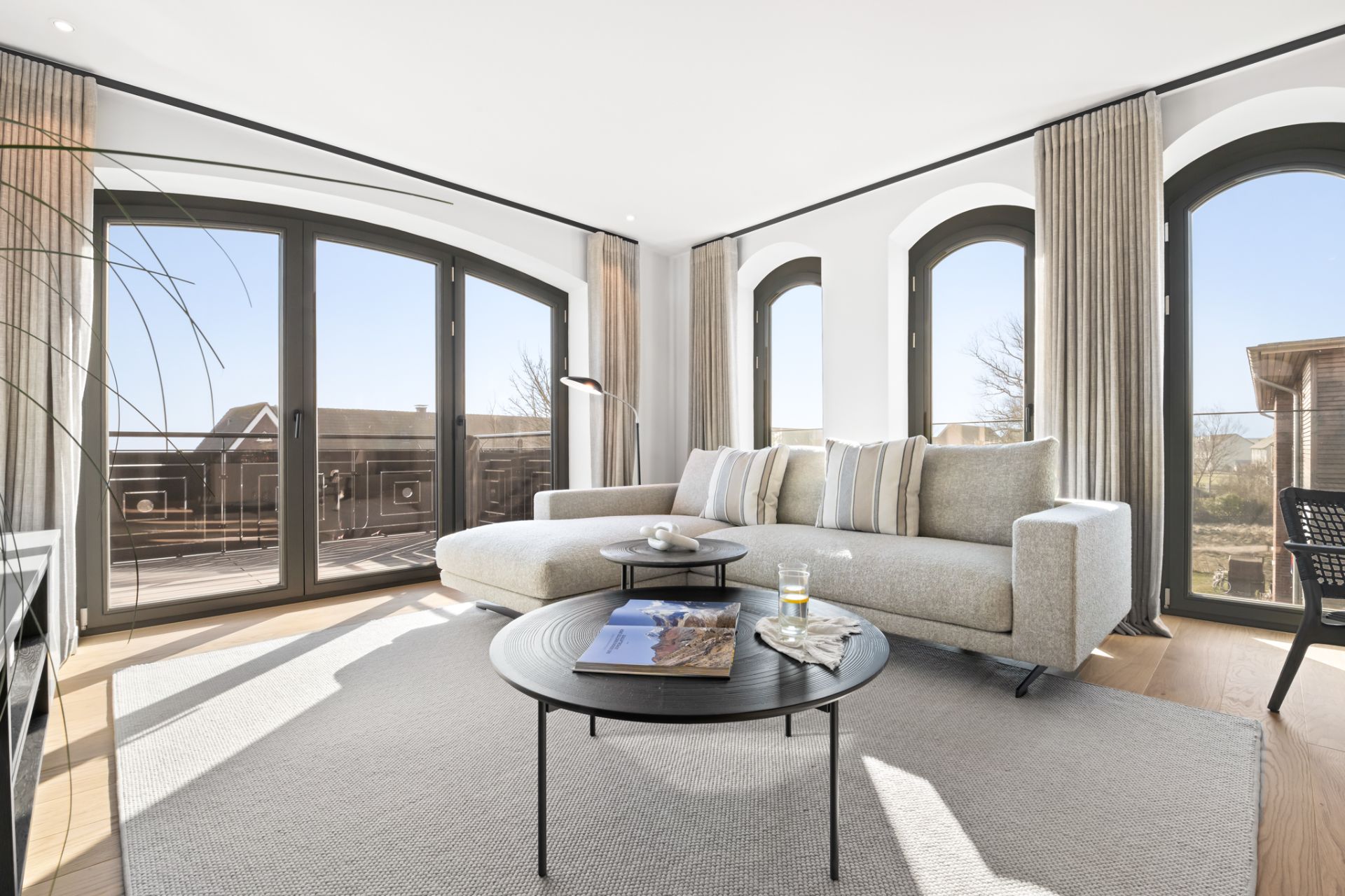 Helles Wohnzimmer mit großem Ecksofa, Couchtisch und bodentiefen Fenstern zu einer Terrasse.