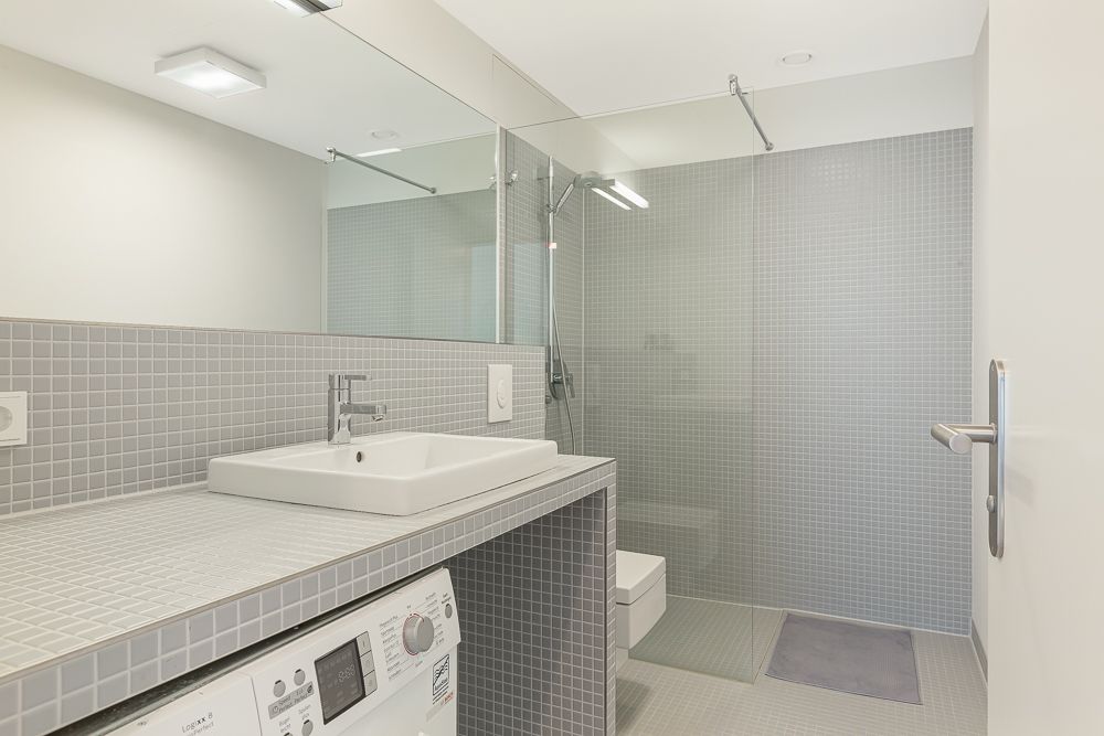 Modernes Badezimmer mit großer Dusche, Waschbecken, Spiegel und Waschmaschine.