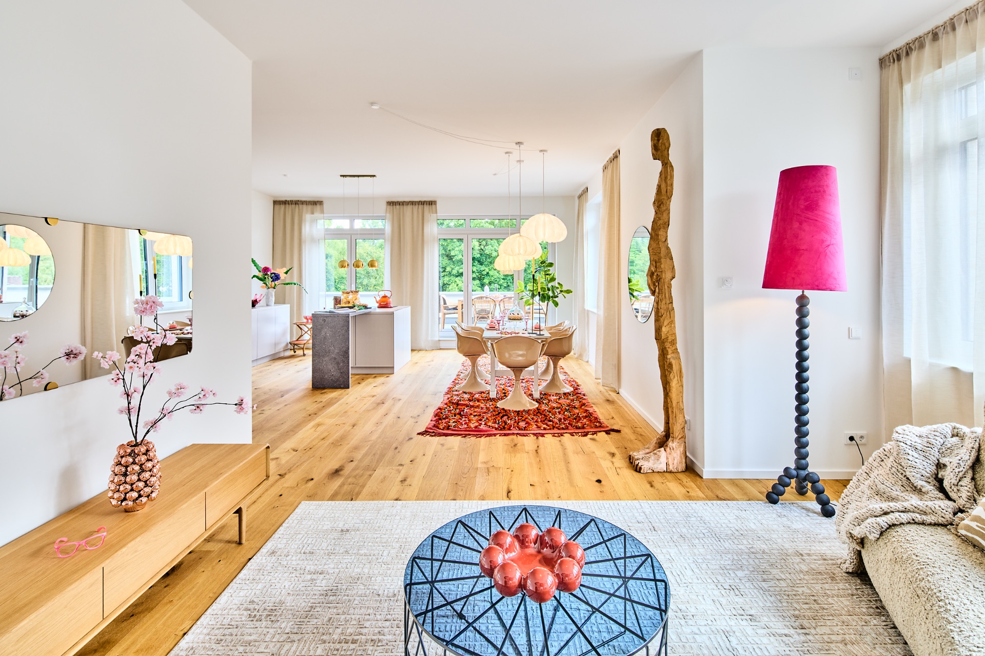 Modernes Wohnzimmer mit Holzboden, hellen Möbeln, großem Fenster und roter Stehlampe.
