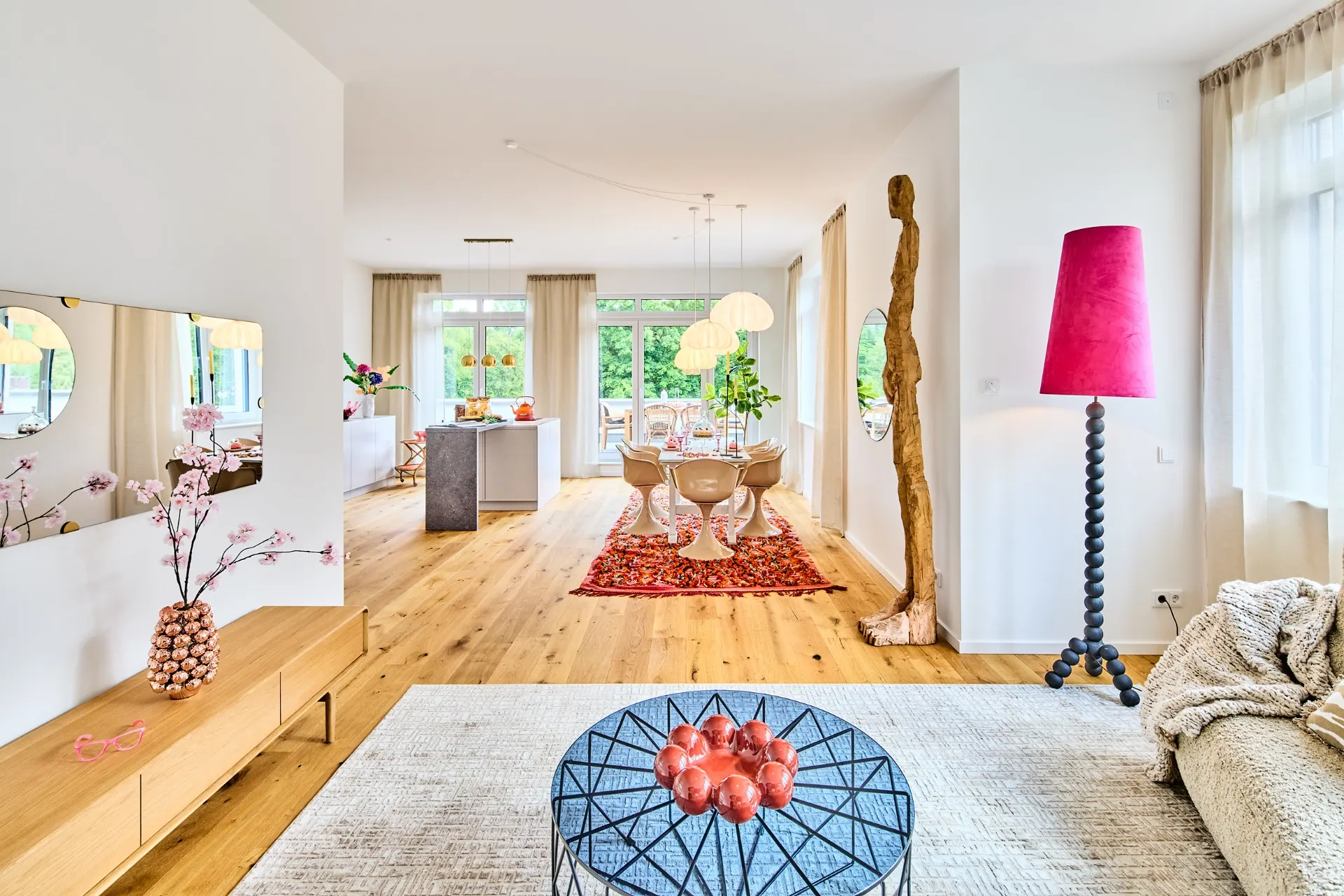 Modernes Wohnzimmer mit Holzboden, hellen Möbeln, großem Fenster und roter Stehlampe.