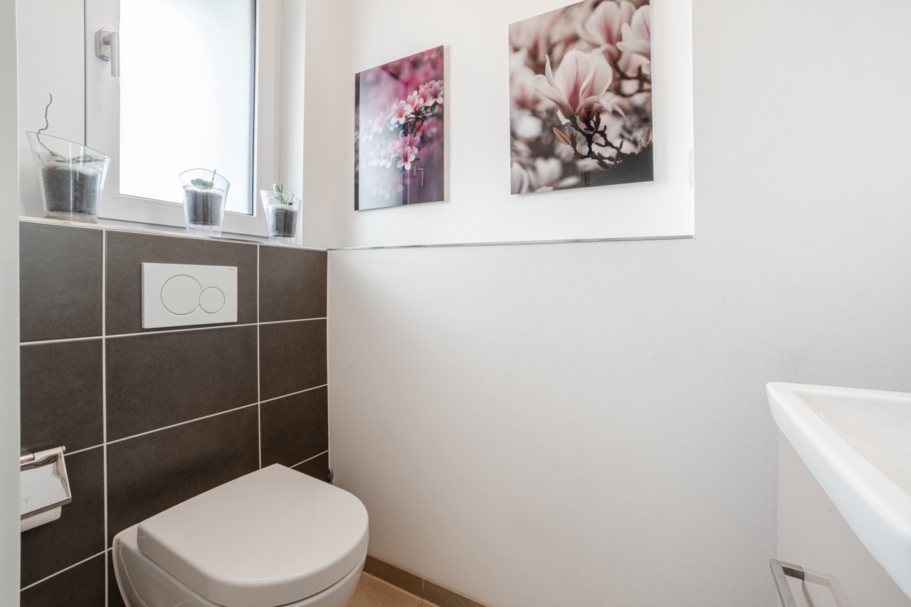 Kleines Badezimmer mit Toilette, Waschbecken, Fenster und zwei Blumenbildern an der Wand.