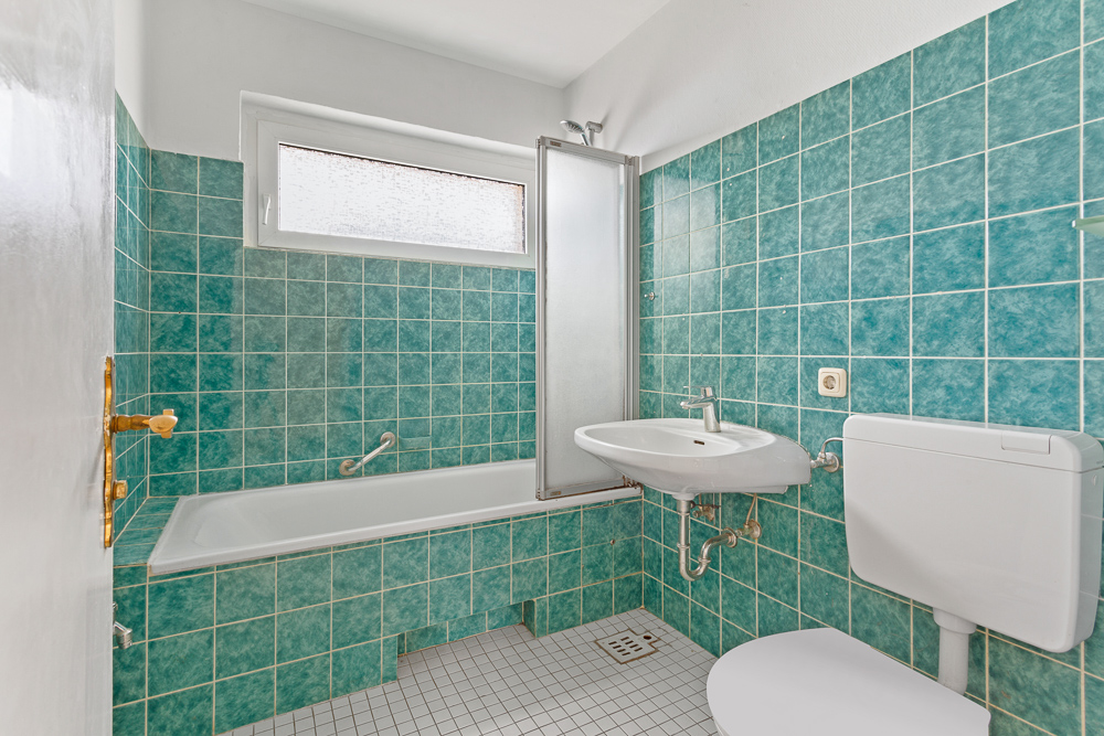 Kleines Badezimmer mit Badewanne, Waschbecken, Toilette und türkisfarbenen Fliesen.