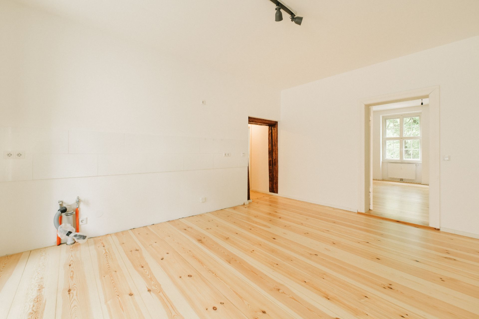 Leerer Raum mit hellem Holzfußboden, weißen Wänden und offenem Durchgang zu einem weiteren Zimmer.