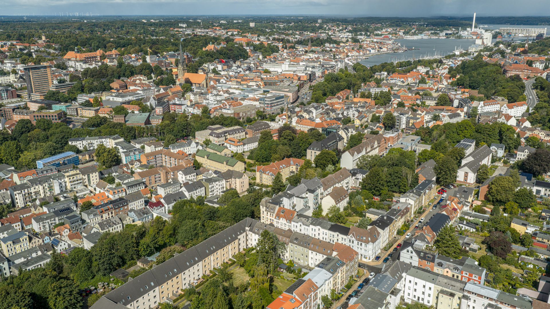 Luftaufnahme eines Wohngebiets mit vielen Häusern, Bäumen und einer nahegelegenen Wasserfläche.