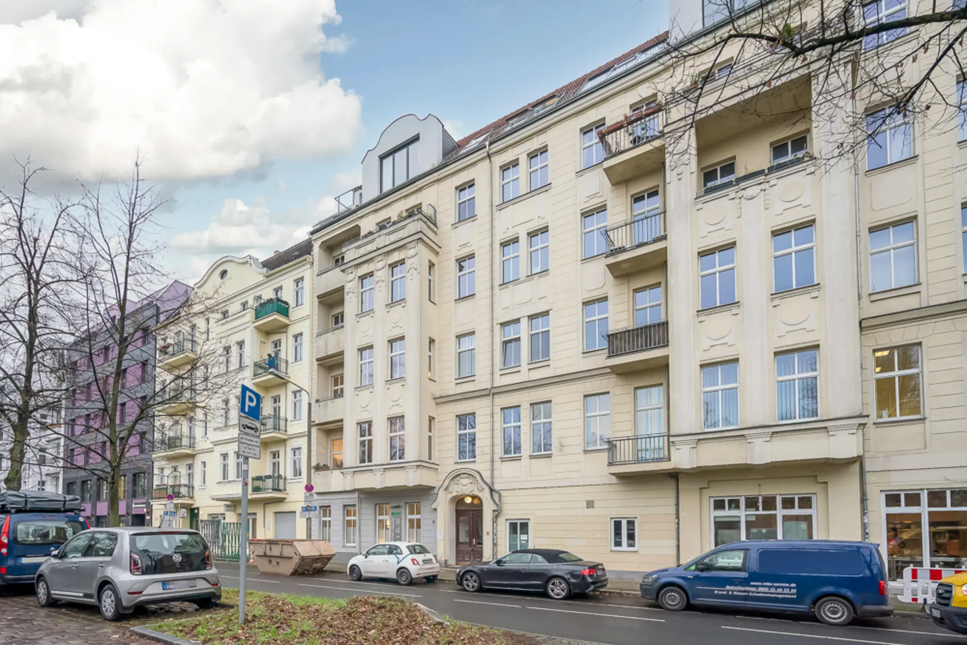Mehrstöckiges Wohnhaus mit Balkonen und geparkten Autos an der Straße.