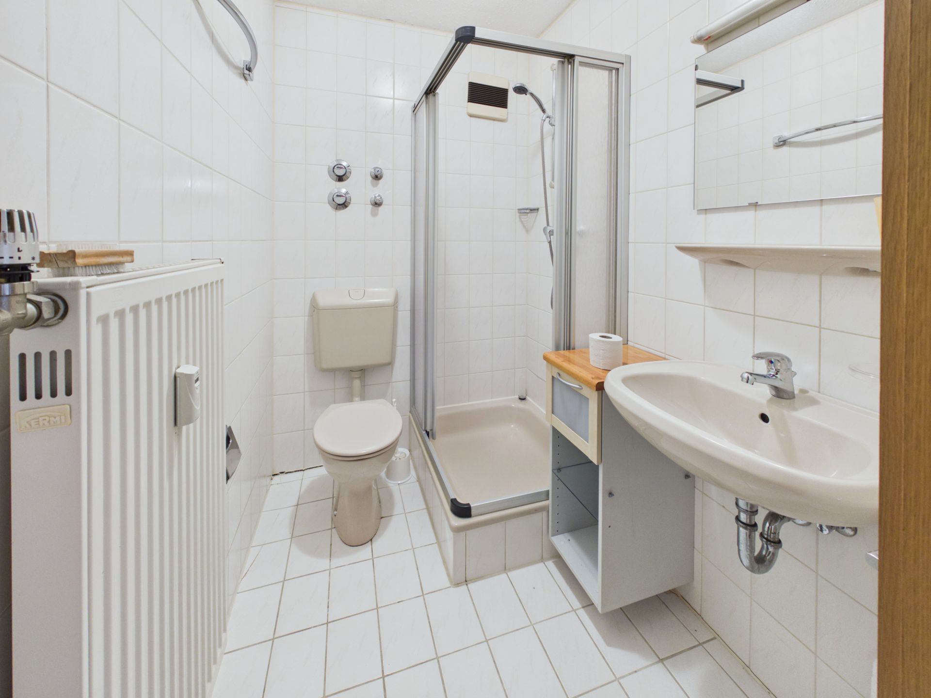 Helles Badezimmer mit Dusche, Toilette, Waschbecken und Heizkörper.