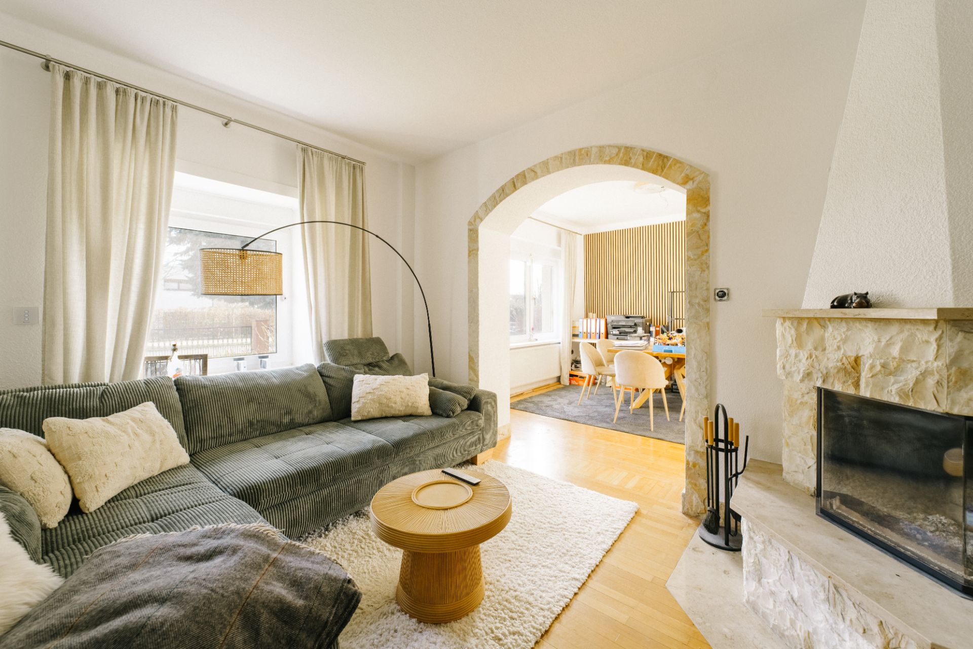Wohnzimmer mit grauem Sofa, rundem Holztisch, Kamin und Blick ins Esszimmer.