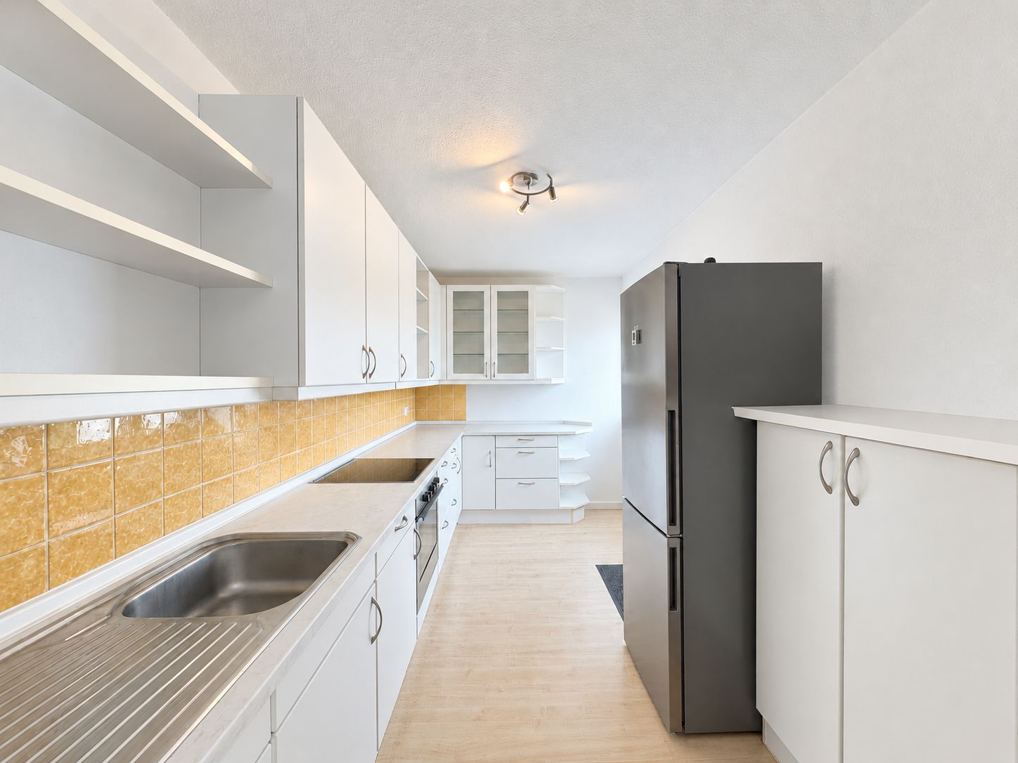 Moderne weiße Küche mit gelben Fliesen, Spüle, Herd und grauem Kühlschrank.