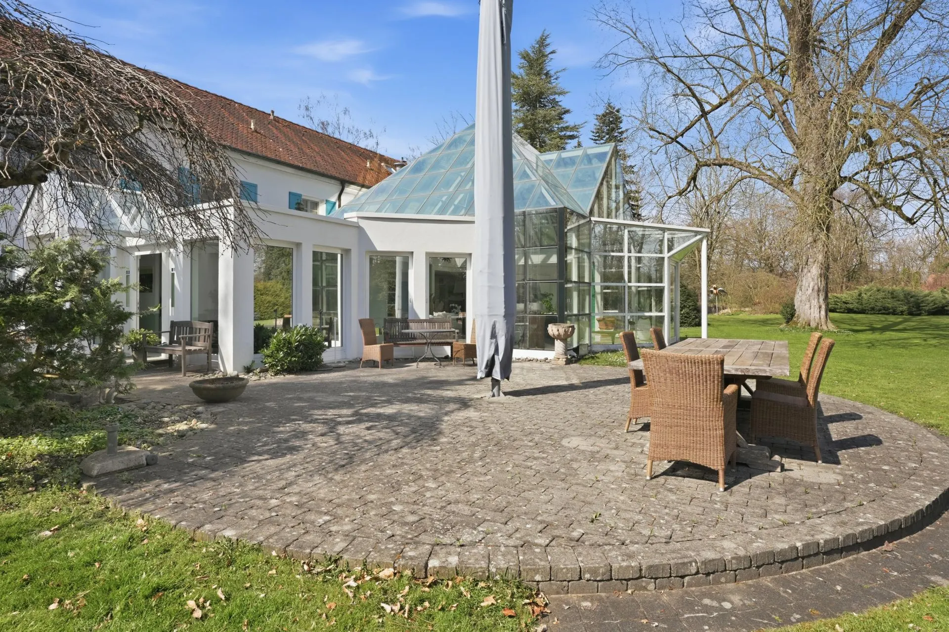 Steinterrasse mit Gartenmöbeln vor einem Haus mit Wintergarten und großem Garten.
