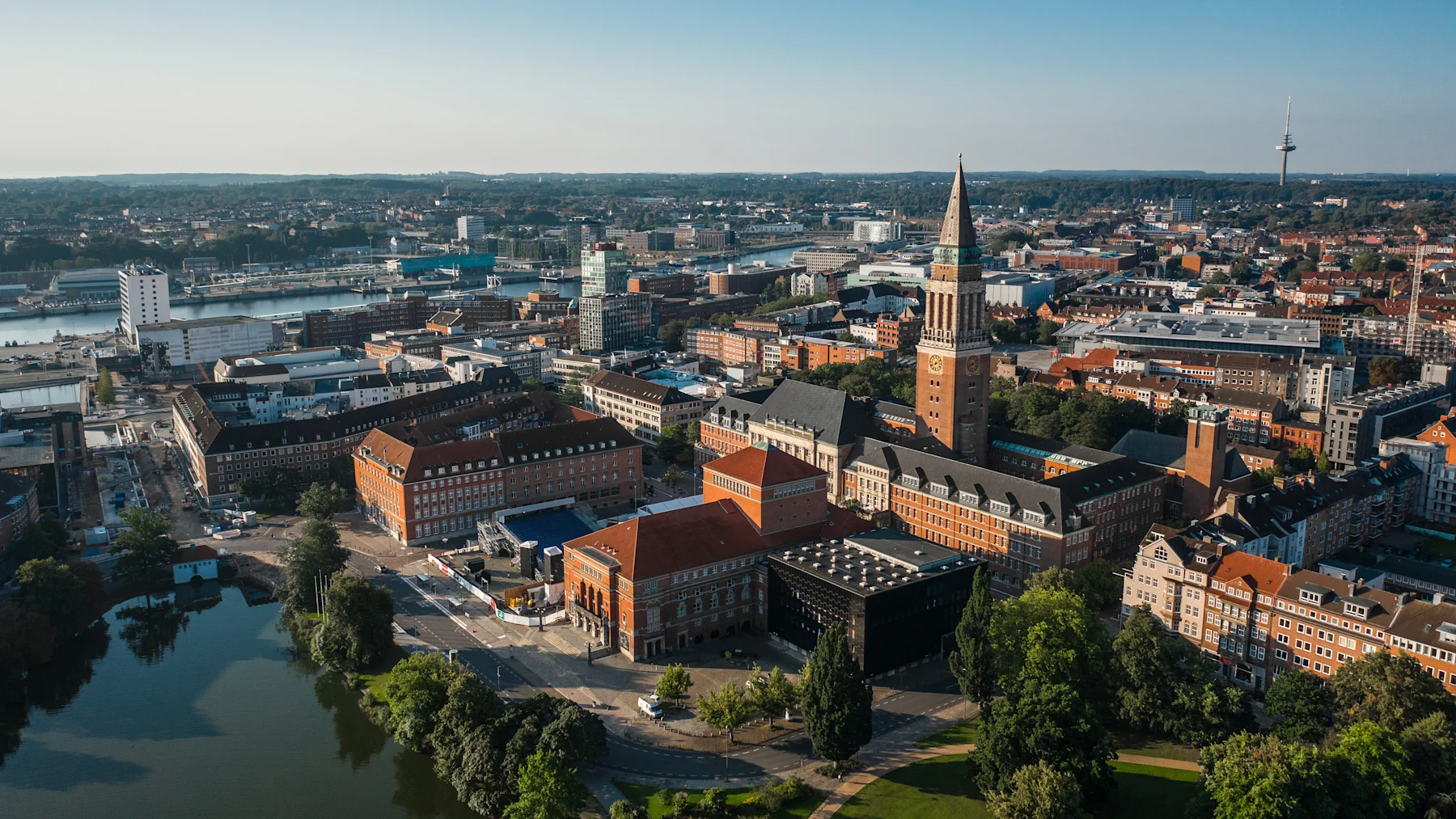 Luftaufnahme einer Stadt mit roten Backsteingebäuden, Kirchturm und einem Park mit See.