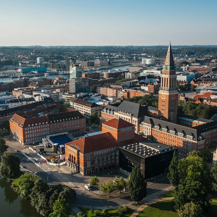 Luftaufnahme einer Stadt mit roten Backsteingebäuden, Kirchturm und einem Park mit See.