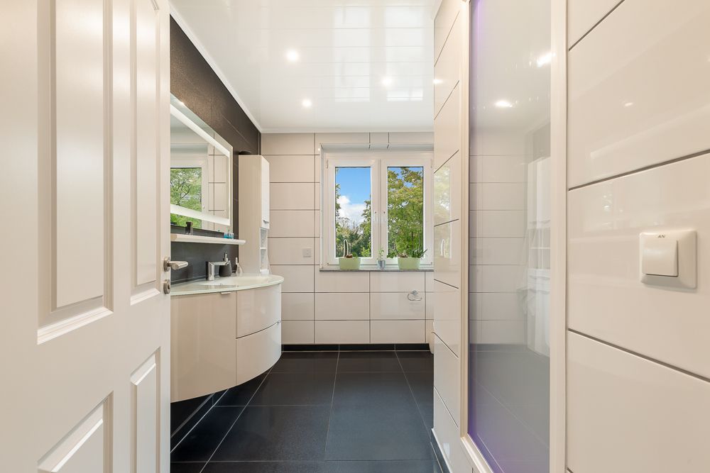 Modernes Badezimmer mit Waschbecken, großem Spiegel und Fenster mit Blick ins Grüne.