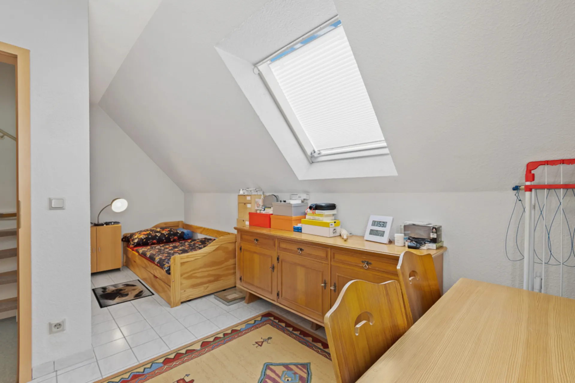 Kleines Zimmer mit schräger Decke, Einzelbett, Kommode, Schreibtisch und Dachfenster.