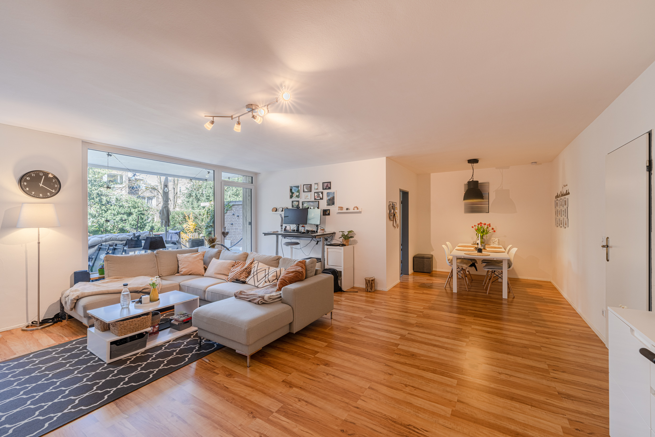Helles Wohnzimmer mit Ecksofa, Esstisch und großem Fenster zum Garten.