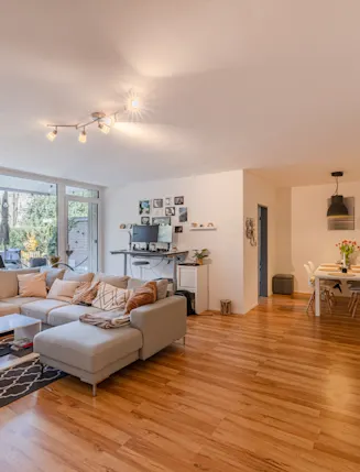 Helles Wohnzimmer mit Ecksofa, Esstisch und großem Fenster zum Garten.