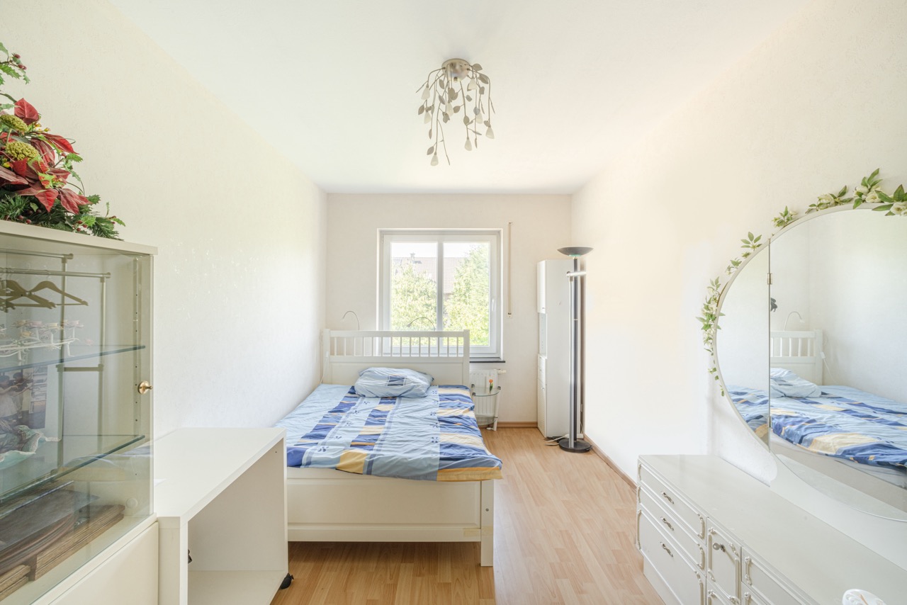 Helles Schlafzimmer mit Einzelbett, Kleiderschrank, Spiegel und Fenster mit Blick ins Grüne.