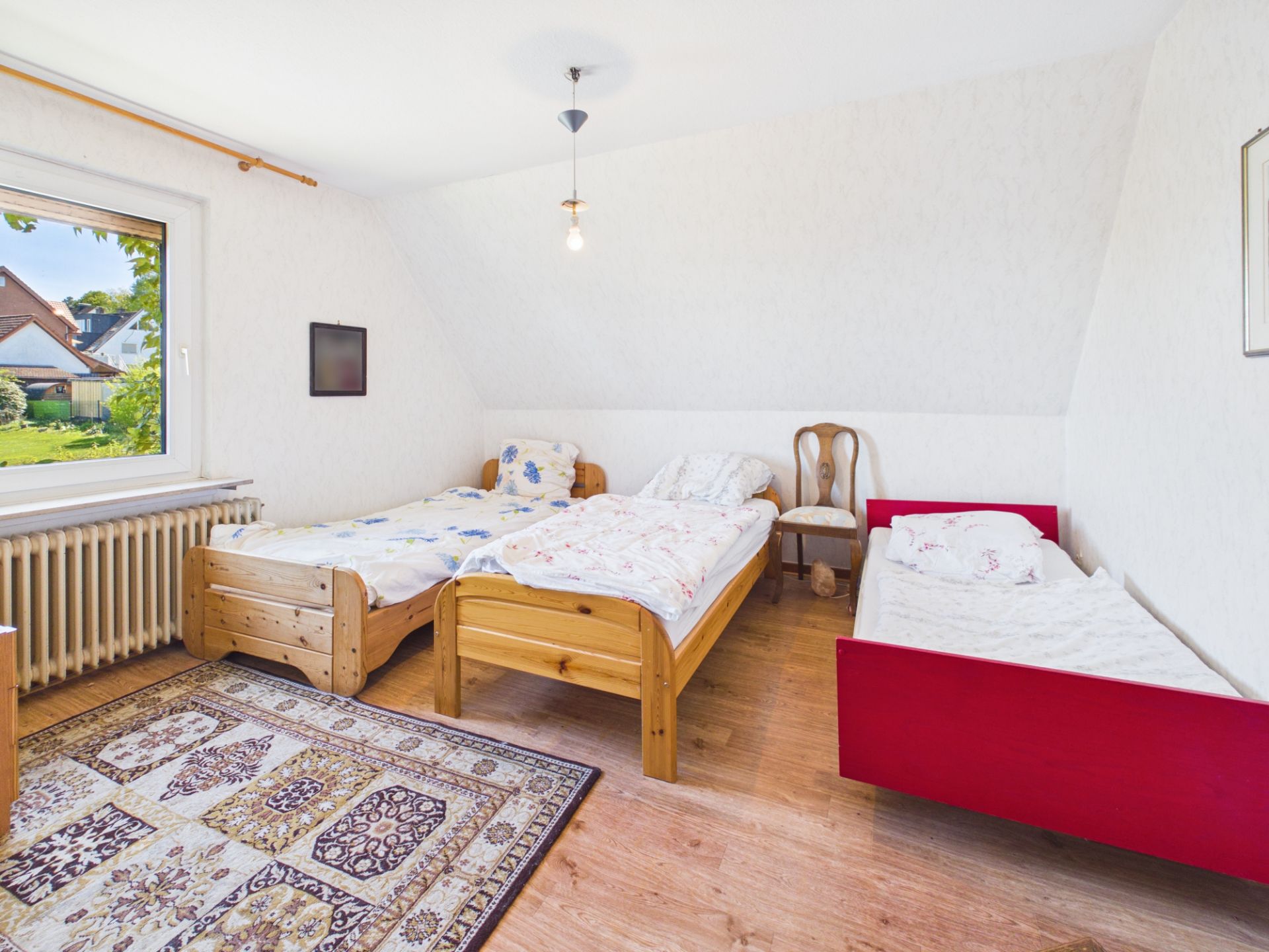 Helles Schlafzimmer mit drei Einzelbetten, Teppich und großem Fenster.