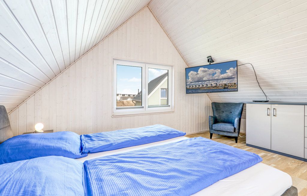 Helles Schlafzimmer mit zwei Betten, blauem Bettzeug, Fenster, Sessel und Wandfernseher.
