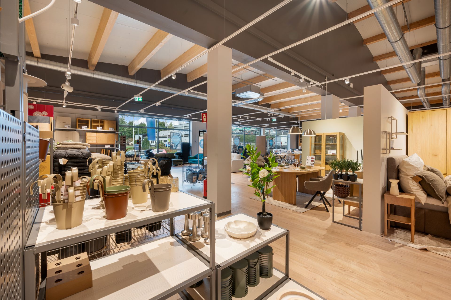 Modern eingerichteter Raum mit Regalen, Blumentöpfen, Sofas und Holzdeckenbalken.