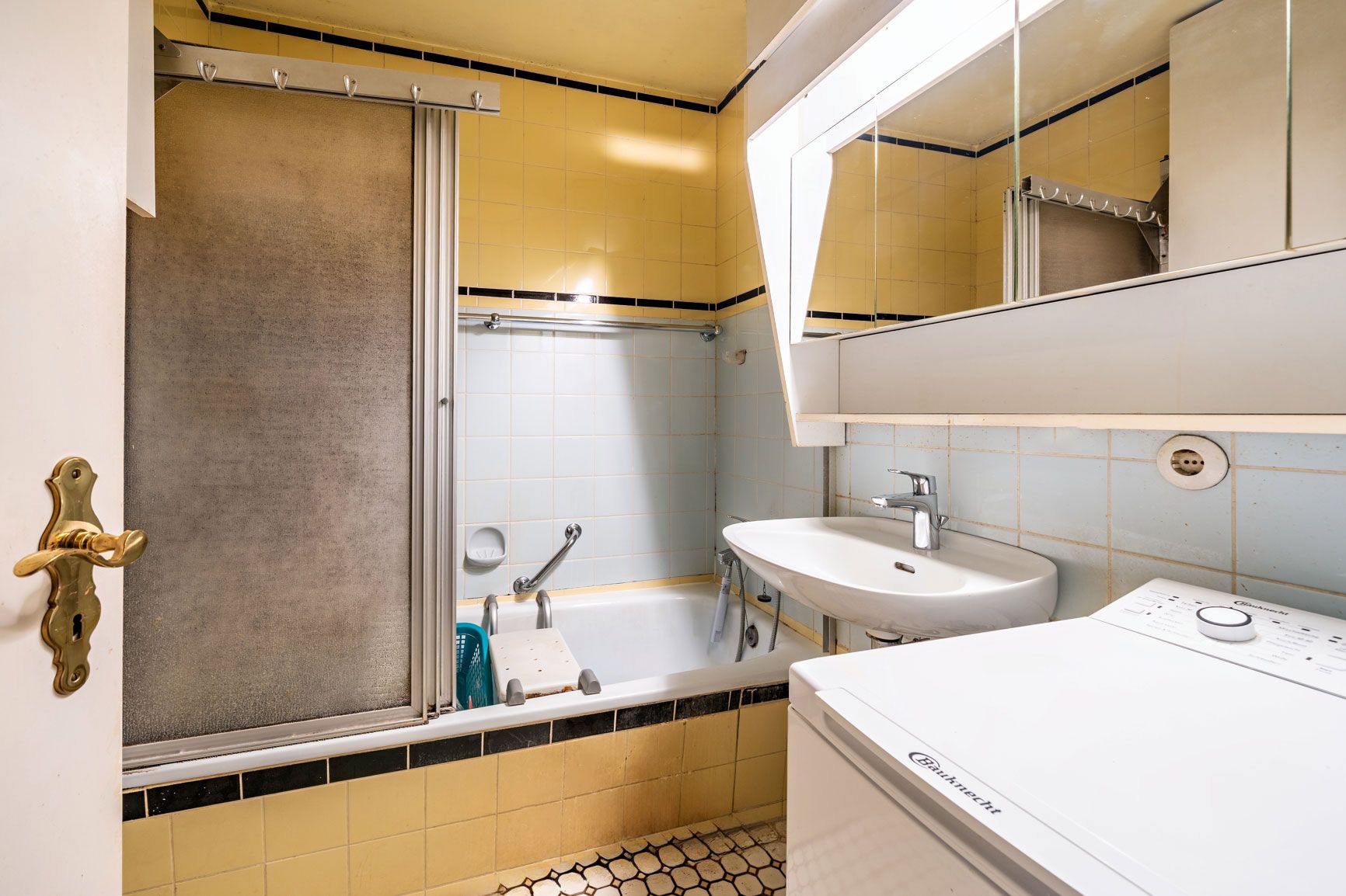 Kleines Badezimmer mit gelben Fliesen, Badewanne, Waschbecken, Spiegel und Waschmaschine.