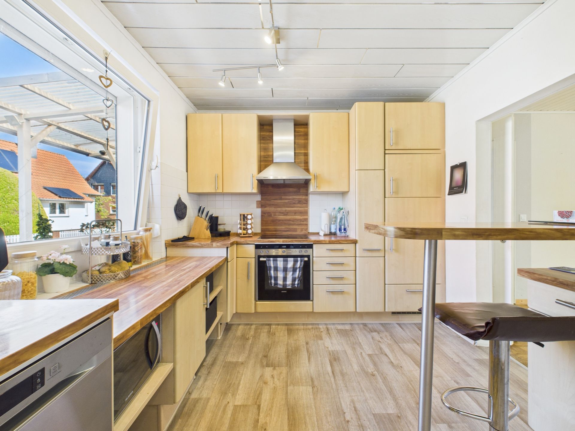 Helle, moderne Küche mit Holzschränken, großem Fenster und Bartisch mit Hockern.
