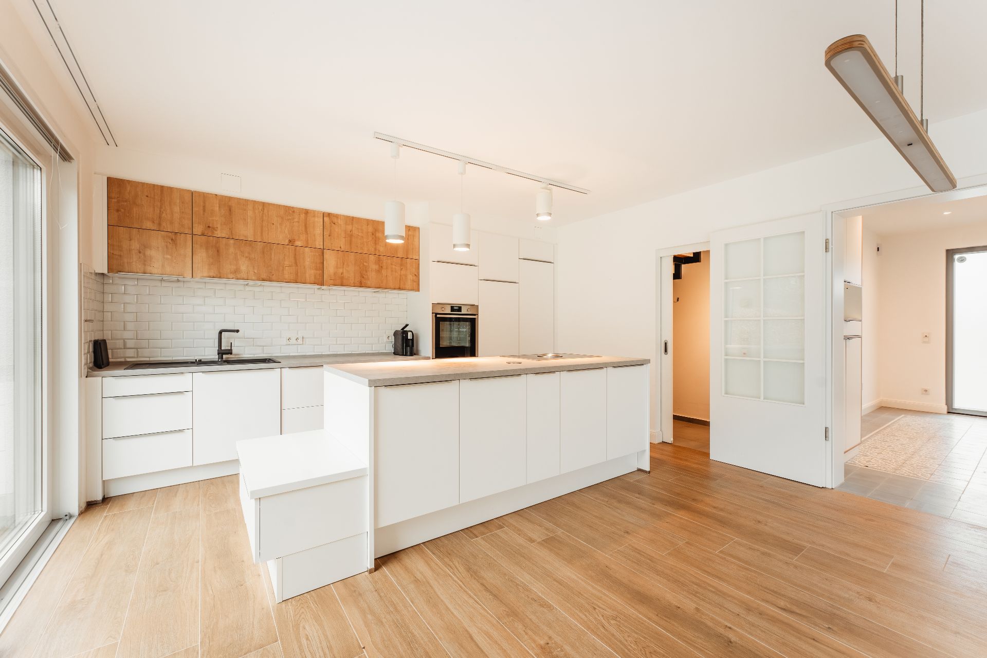 Moderne Küche mit Kücheninsel, weißen Schränken und Holzfronten auf hellem Holzboden.