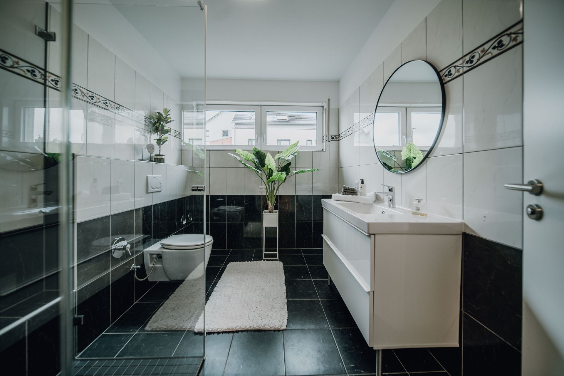 Modernes Badezimmer mit großem Spiegel, Dusche, WC, Waschbecken und Pflanzen.