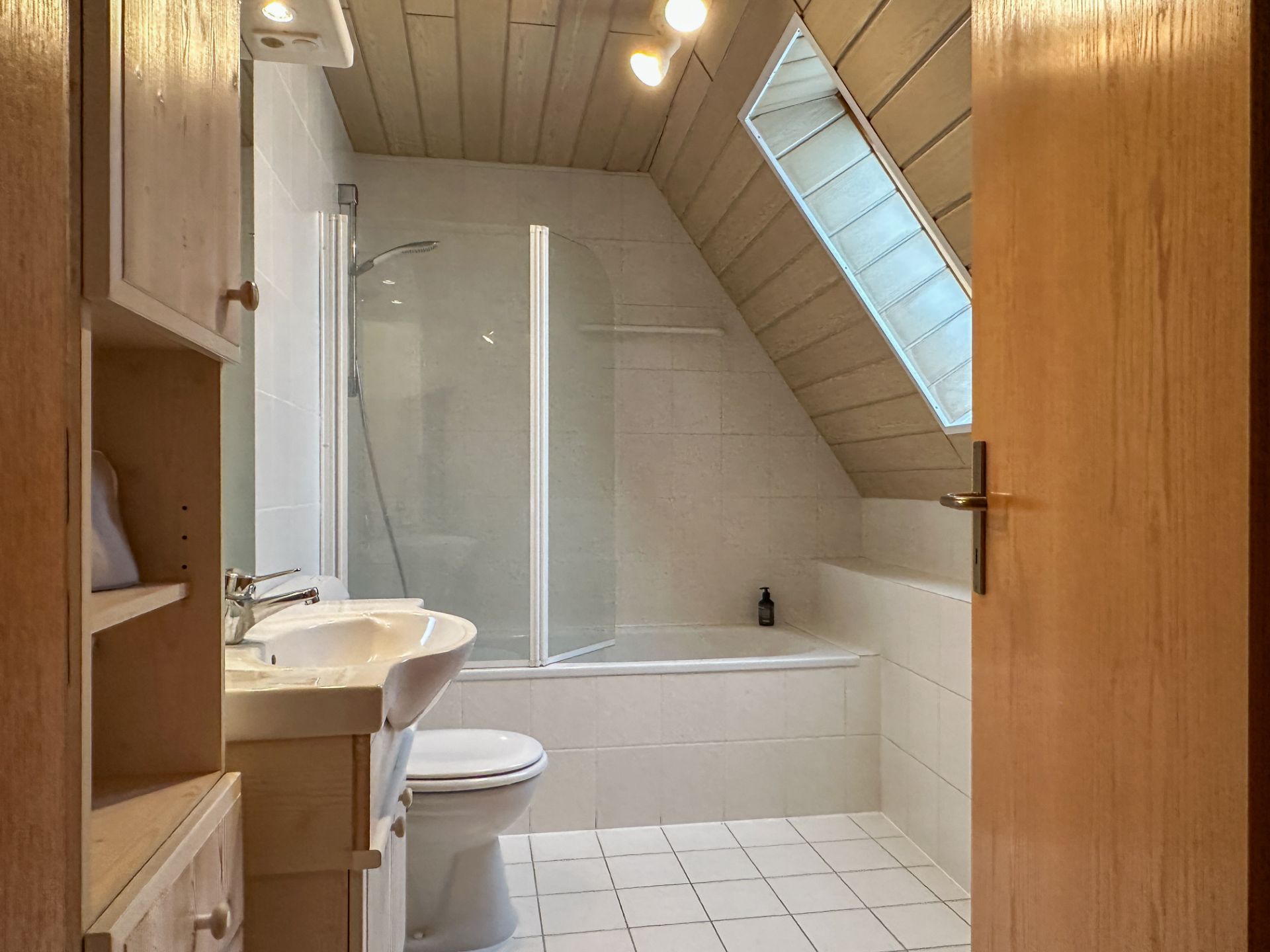 Badezimmer mit Dachschräge, Badewanne, Waschbecken, Toilette und Fenster.